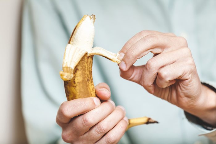 Male hand in a shirt holding a ripe banana and clean it