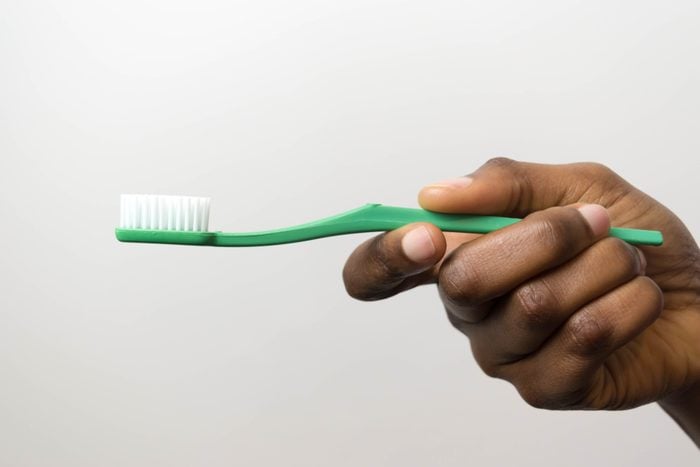 Clsoe up of green toothbrush in dark brown skin hand isolated on white background hand of African American young girl holding toothbrush.