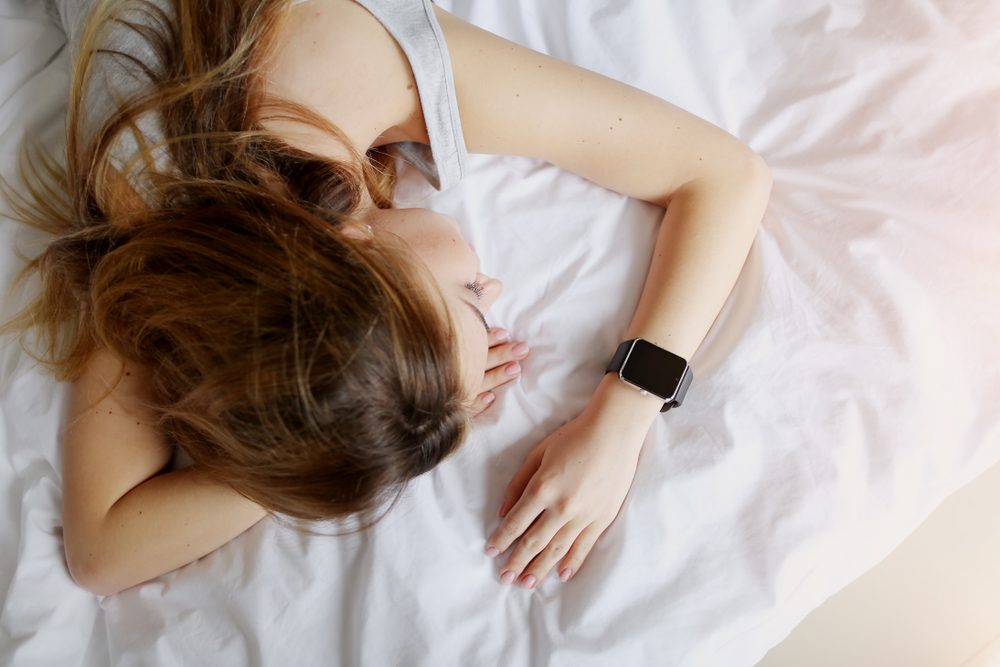 woman sleeping at white bed tracking function on smartwatches information on deep fitful sleep. concept of measure brain waves, eye movement and several breathing metrics for health