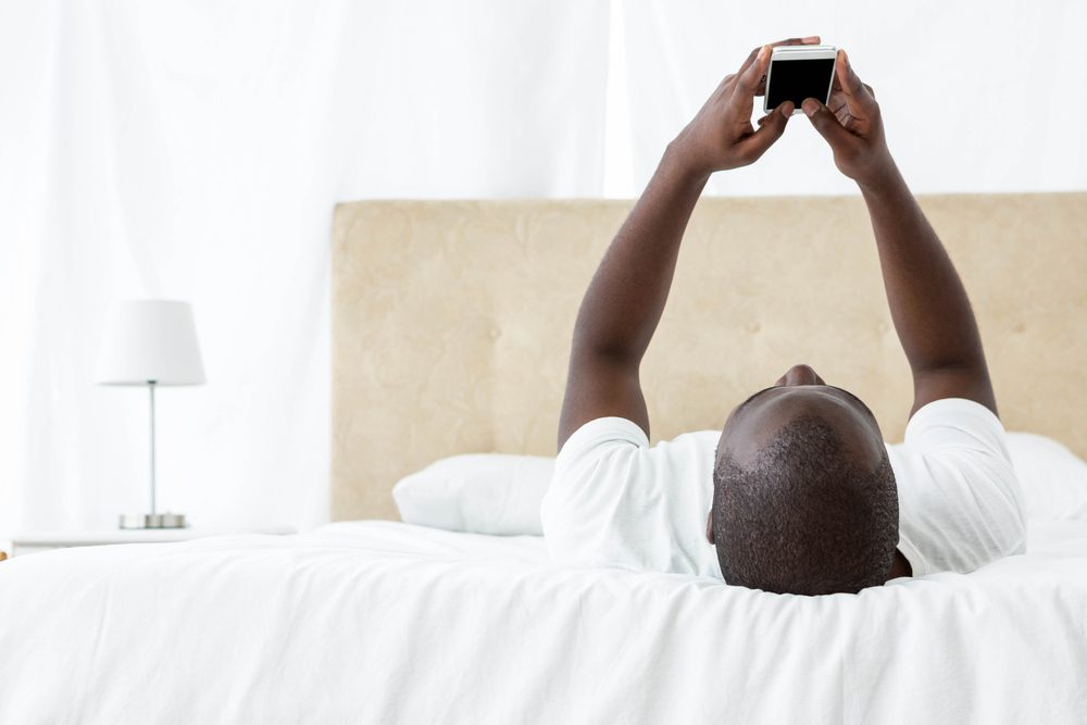 Man lying on bed and text messaging on mobile phone at home