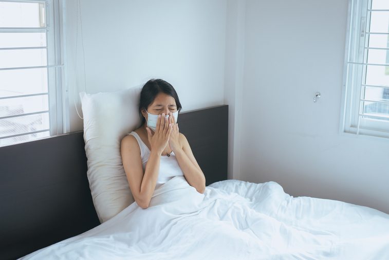 Concept of health woman using protective mask with cold blowing and runny nose on bed,sick woman sneezing