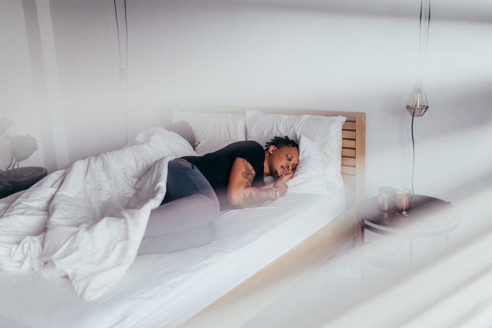 Uomo africano che dorme in camera da letto con donna dietro. Coppia che dorme schiena a schiena sul letto.