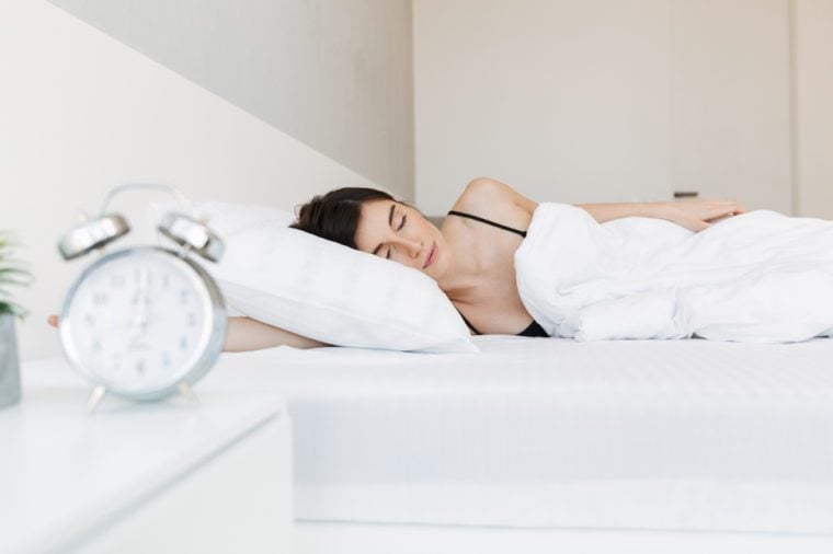 Portrait of a beautiful young woman sleeping in bed at the bedroom with alarm clock on a nightstand