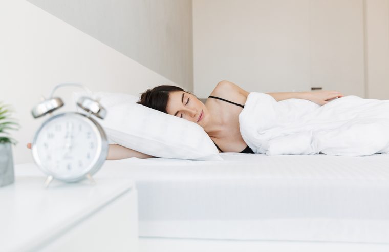 Portrait of a beautiful young woman sleeping in bed at the bedroom with alarm clock on a nightstand