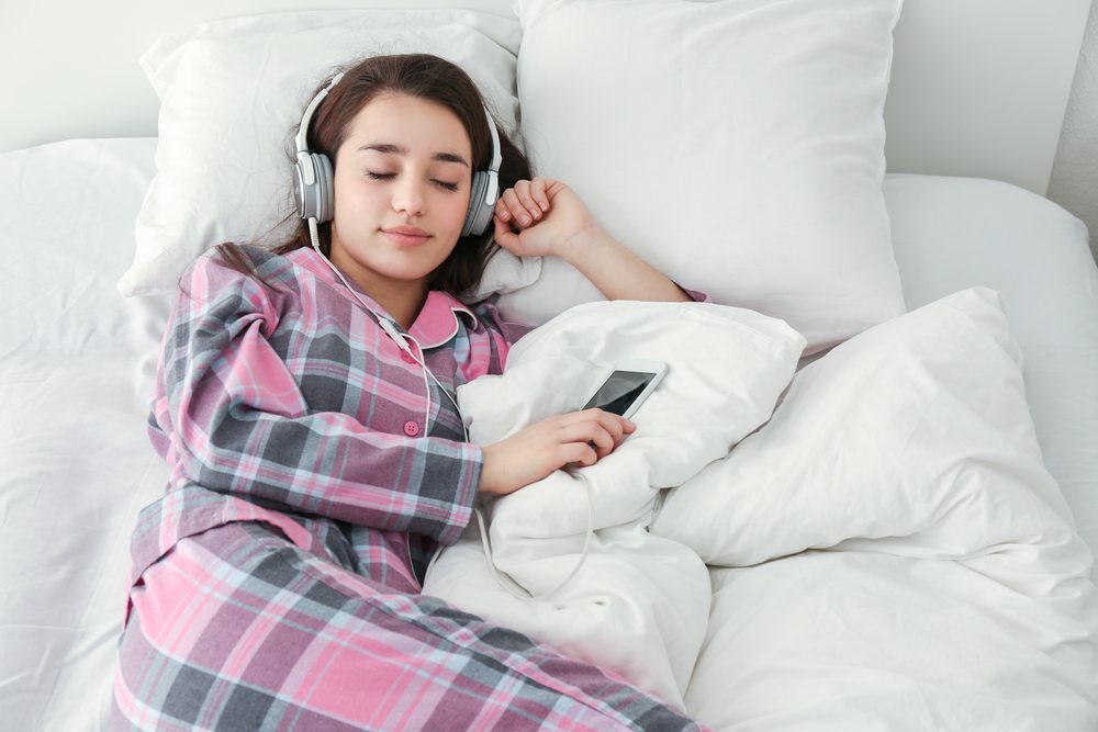 Young woman listening to music in headphones on bed