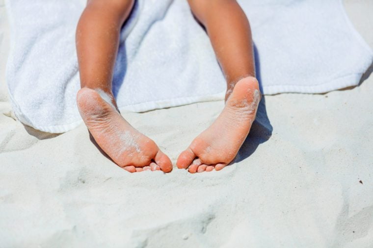 Close up of child feet on beach towel on tropical white beach