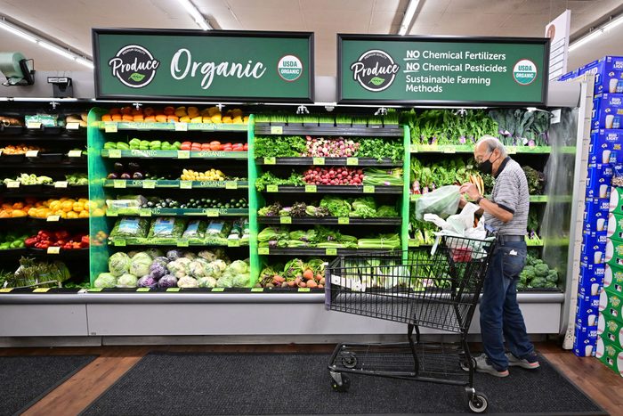 man shopping in the organic produce section of a grocery store with a cart