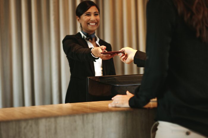 Smiling female concierge returning the documents to hotel guest after check-in process. Female client receiving her documents at hotel reception desk after check-in.