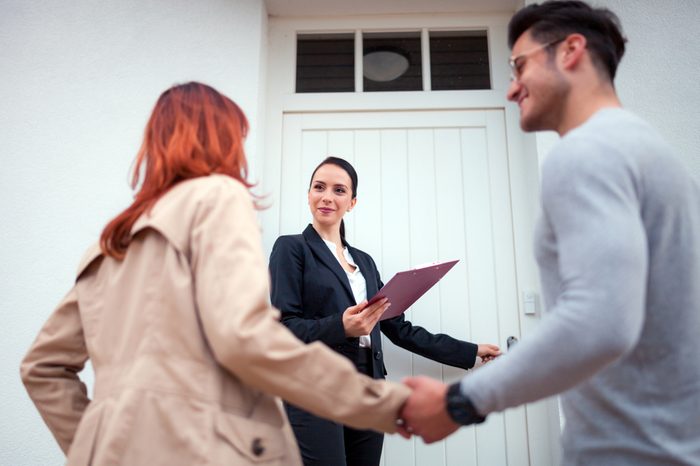 Real estate agent near door inviting young couple to enter house for visit