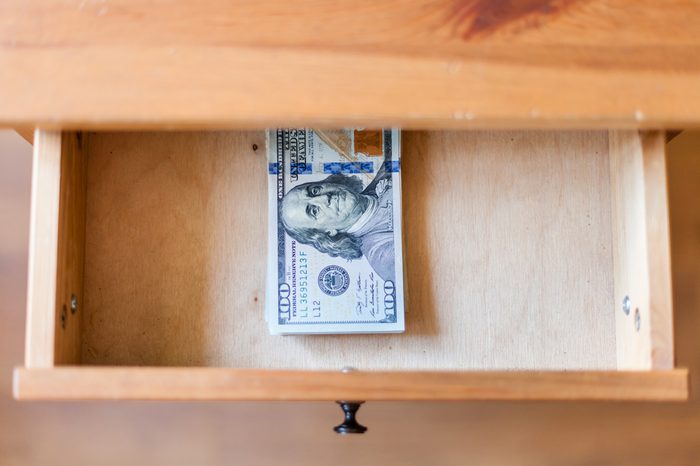 top view of hundred-dollar bills pack in open drawer of nightstand