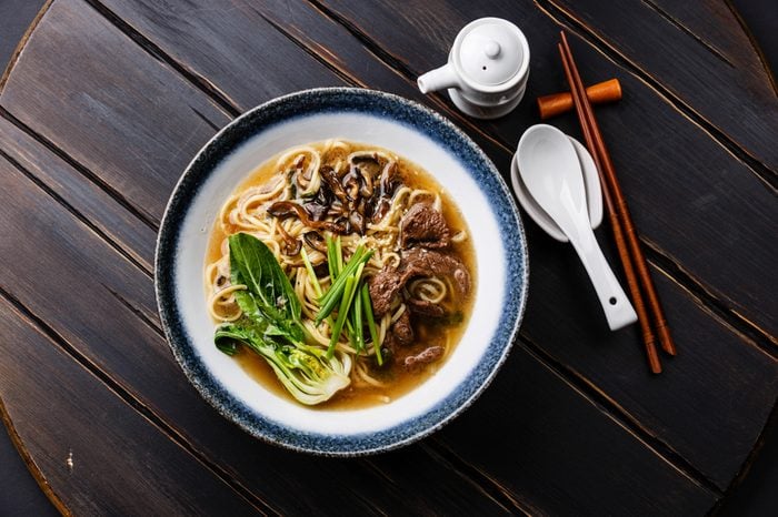Ramen asian noodle in broth with Beef and Oyster mushrooms in bowl on dark wooden background