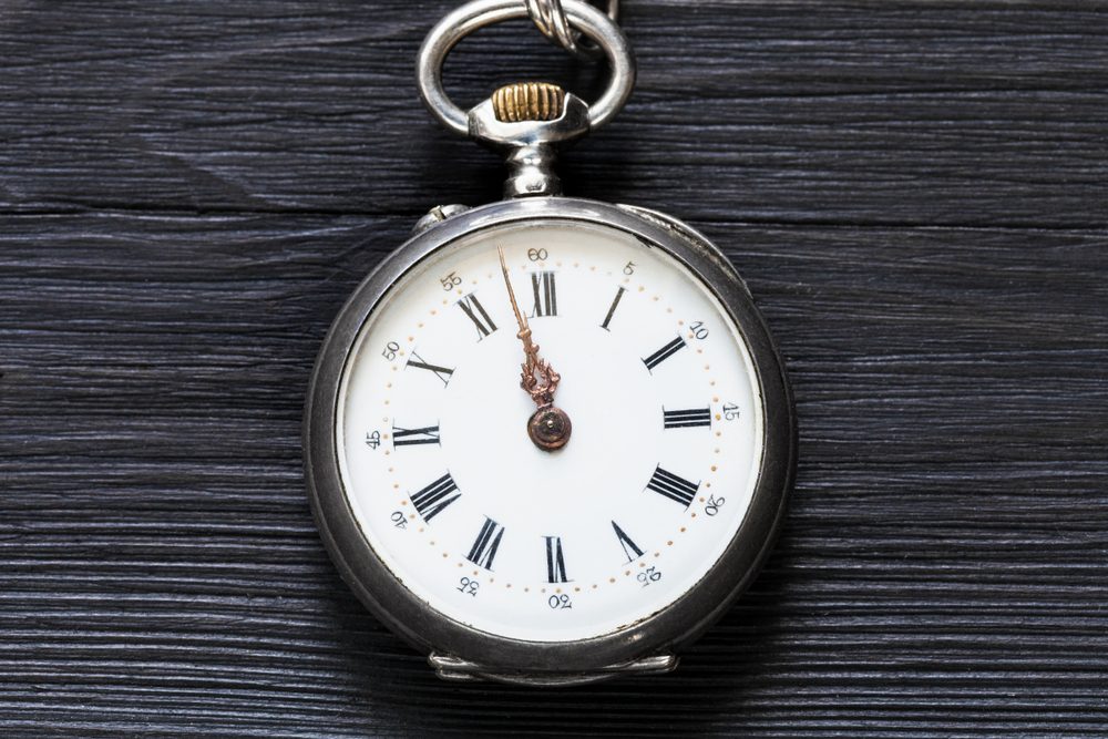 two minutes to twelve o'clock on vintage pocket watch on black wooden background