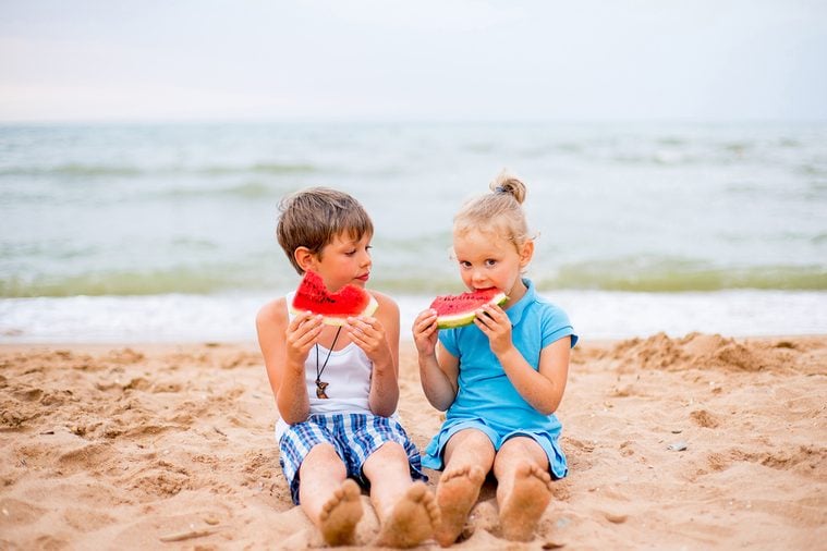two children eating watermelon on the beach