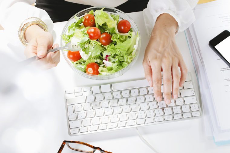 Young businesswoman eating a salad while working in office. /Young businesswoman typing on the laptop.