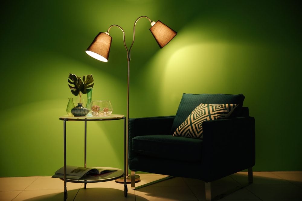 Armchair, lamp and table with home decor on green wall background
