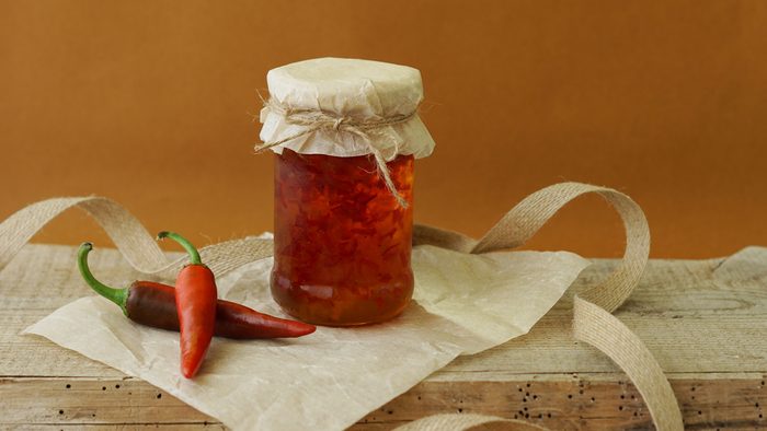 Pepper chili jam in jar on paper and wooden background