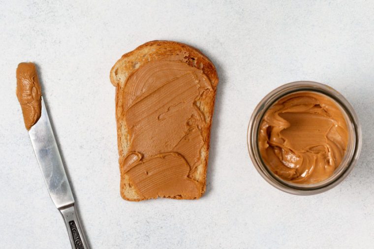 toast with peanut butter, jar of peanut butter, knife on a light gray background. view from above