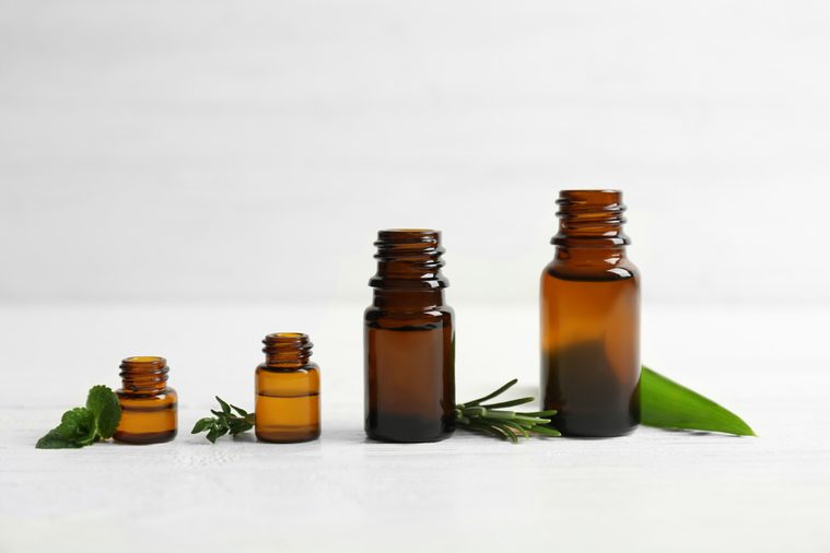 Bottles with essential oils and fresh herbs on light background