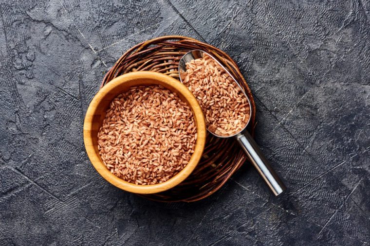 Wild brown rice in wooden bowl on black background. Top view of grains.