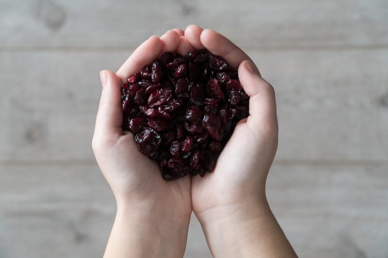 Female hands filled with dried cranberries on a bright wooden background.