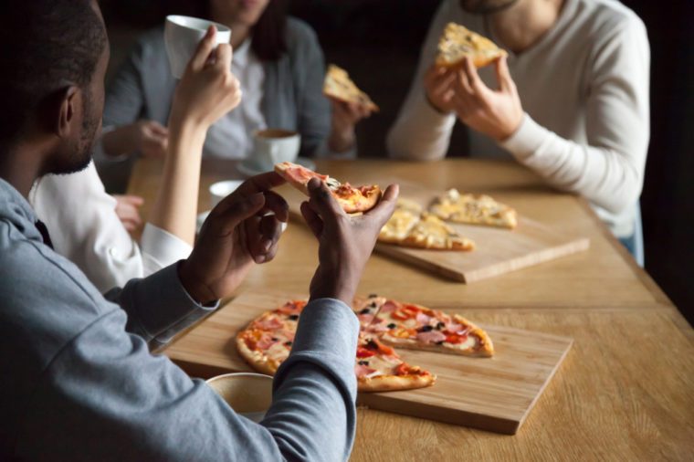 Close up of diverse friends hang out in pizzeria enjoy pizza and coffee, multiethnic young people talk having fun in Italian restaurant eating tasty food, millennial colleagues meet in café for lunch