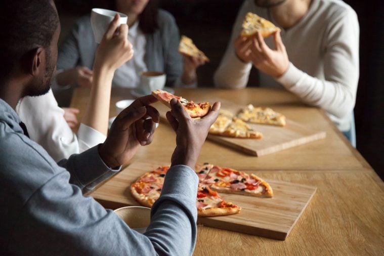 Close up of diverse friends hang out in pizzeria enjoy pizza and coffee, multiethnic young people talk having fun in Italian restaurant eating tasty food, millennial colleagues meet in café for lunch