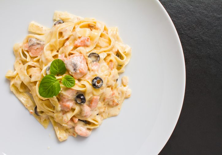 Salmon pasta shot with creamy sauce and olives on white plate. See more italian and healthy