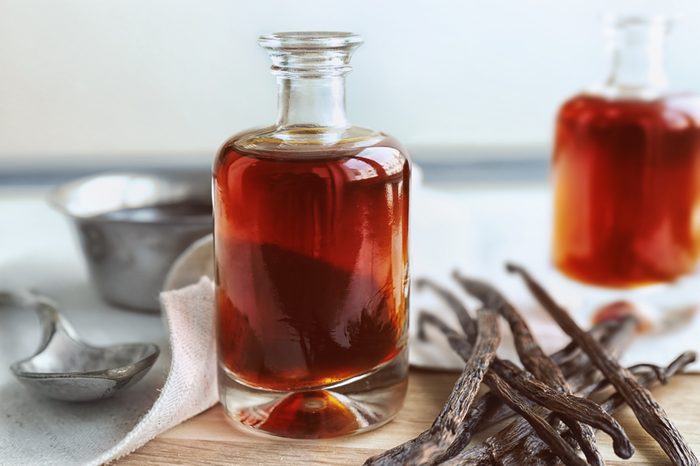 Bottle with aromatic extract and dry vanilla beans on table