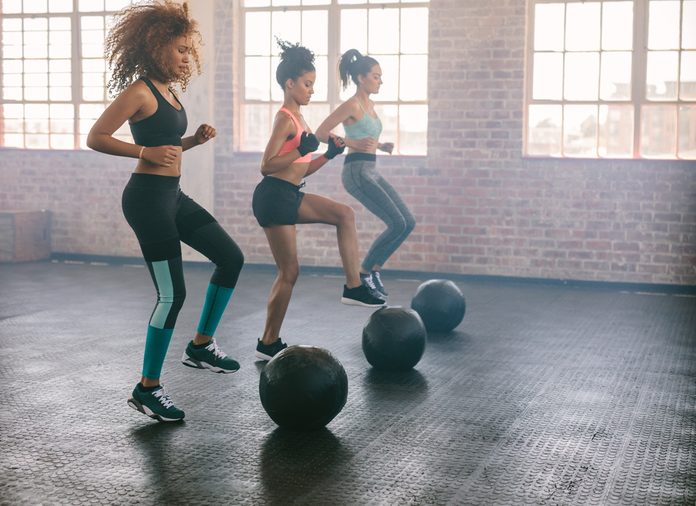 Young women exercising in aerobics class with medicine balls on floor. Three females doing workout together in gym.
