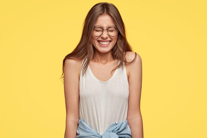 Funny emotive teenager with overjoyed expression, closes eyes from pleasure, laughs at good joke, dressed in casual outfit, isolated over yellow background. People and positive emotions concept