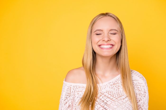 Portrait with copy space empty place of comic funky girl laughing with clenched teeth keeping eyes closed isolated on yellow background