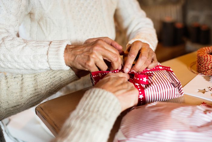 Unrecognizable senior couple in sweaters wrapping Christmas gift.
