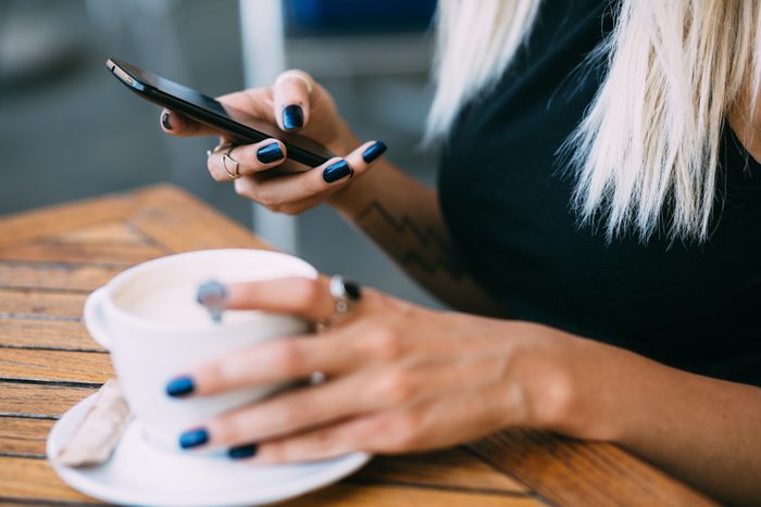 Close up of hip young woman using phone in cafe