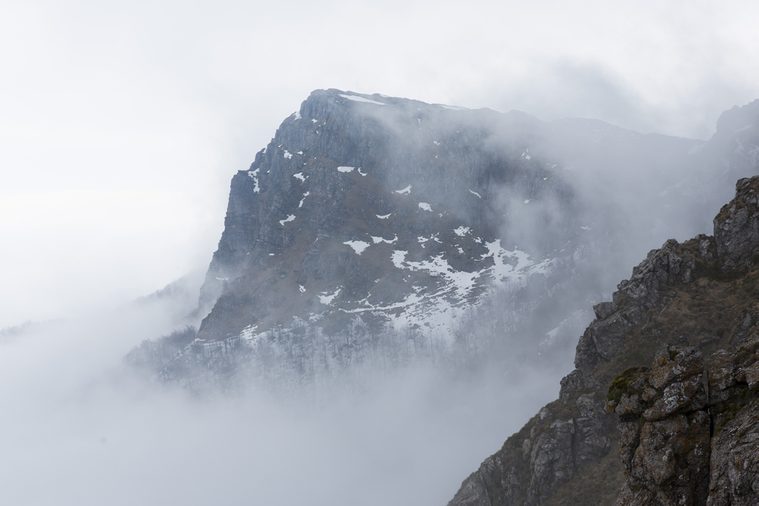 High rocky mountain peak covered with snow and fog.
