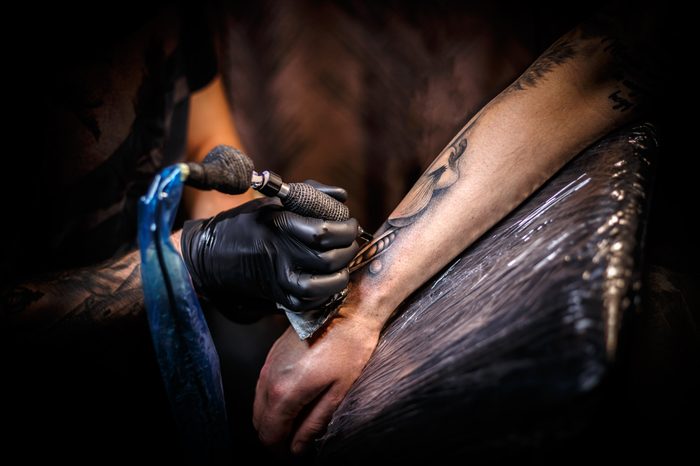 Tattoo artist creating a tattoo on a man's arm.