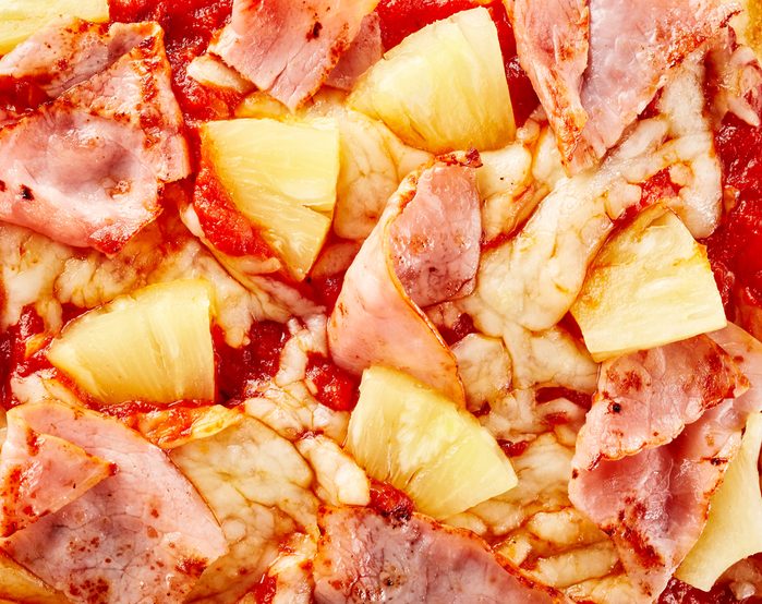 Delicious Hawaiian pizza topping background texture with pineapple and thinly sliced ham on melted mozzarella cheese viewed from above in close up detail