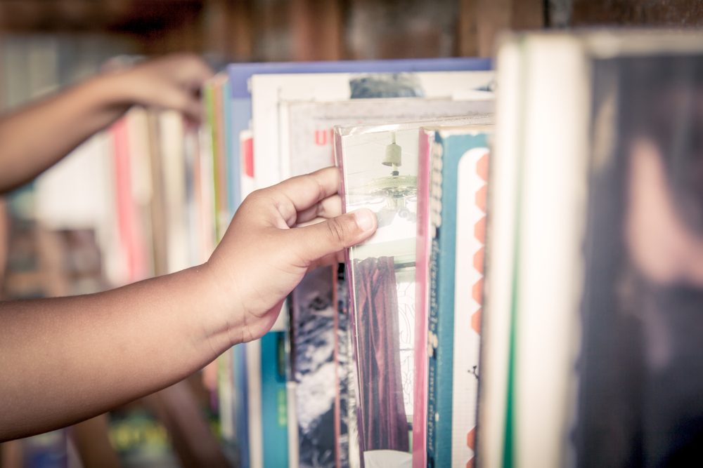 hand of little girl selecting a book from book shelf in vintage color tone