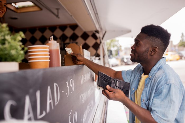 street sale, payment and people concept - happy african american young man buying wok and paying with dollar money at food truck