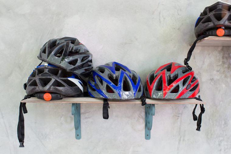 Stack of bicycle helmets on wooden shelf and grange cement wall.