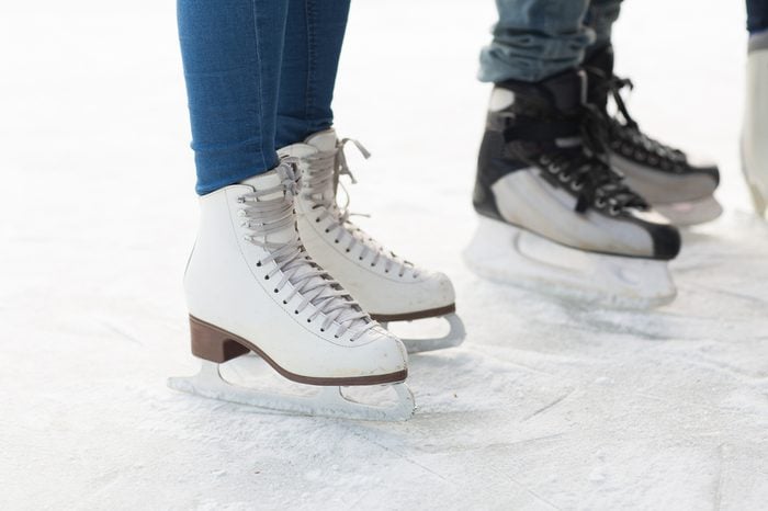 people, winter sport and leisure concept - close up of legs in skates on skating rink