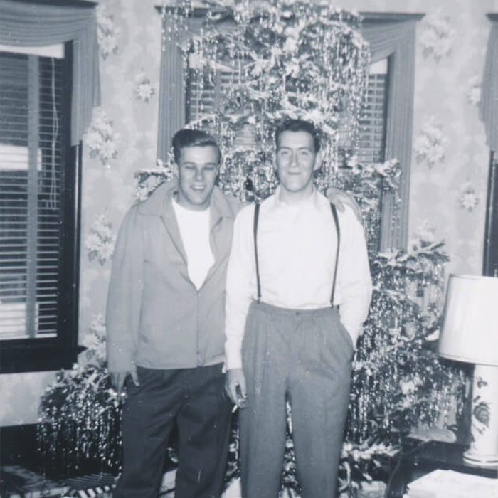 Black and white photo of two men standing in front of a christmas tree