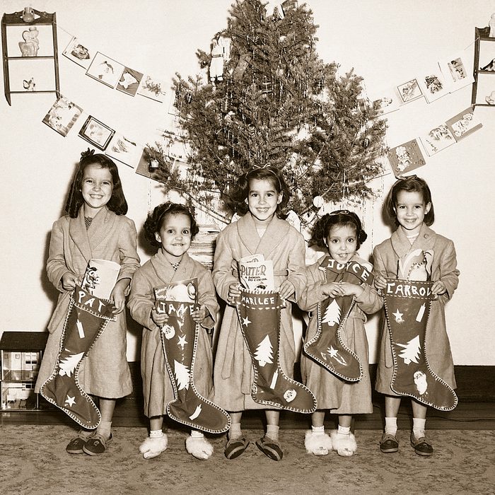 Black and white photo of girls lined up for a photo in front of their Christmas tree with stockings in hand