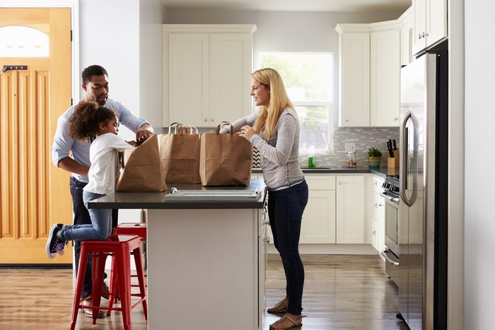 Girl and mixed race parents unpack shopping bags in kitchen