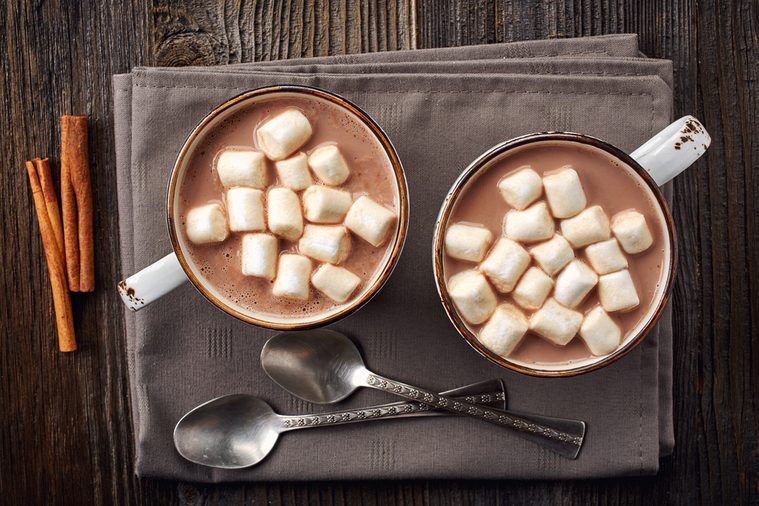 Two cups of hot cocoa with marshmallows and cinnamon sticks on wooden background