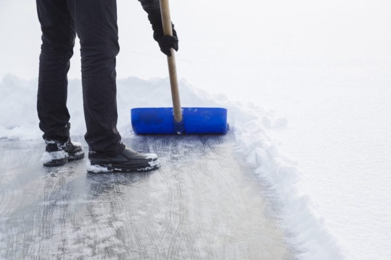 Man cleaning snow with blue shovel from ice surface for ice skating. Winter routine concept.