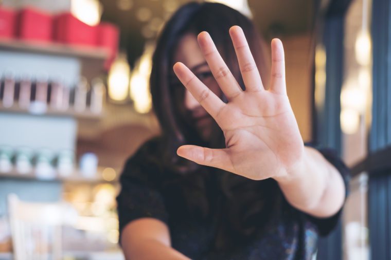 An Asian woman showing her hand sign cover her face to say no to someone with feeling angry in restaurant