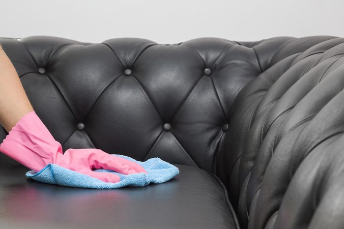 Employee hand in rubber protective glove with microfiber cloth cleaning luxury black leather chester sofa. Upholstered furniture. Early spring or regular clean up. Commercial cleaning company concept.