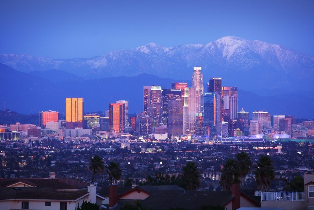 Downtown Los Angeles skyline over snowy mountains at twilight.