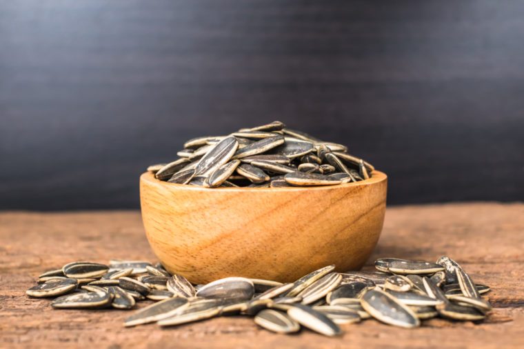 sunflower seeds group with a wooden cup on wood background. The name of science : Helianthus annuus