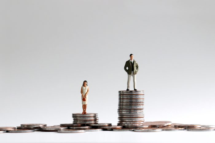 The concept of gender gap between employment and promotion. Miniature people standing on a pile of coins.